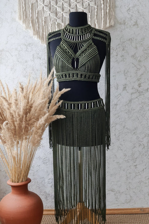 Mannequin wearing a black beaded dress with decorative elements, surrounded by pampas grass against a textured wall.
